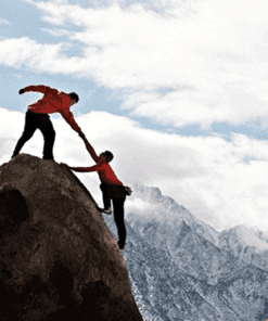 Two people on a rock with one helping another up the side of it.