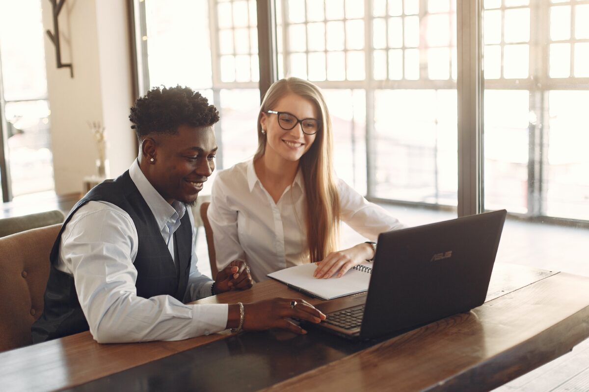 A man and woman sitting at a table looking at a laptop.