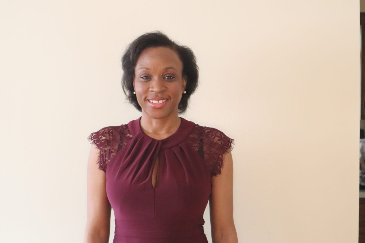 A woman in a maroon dress standing next to a wall.