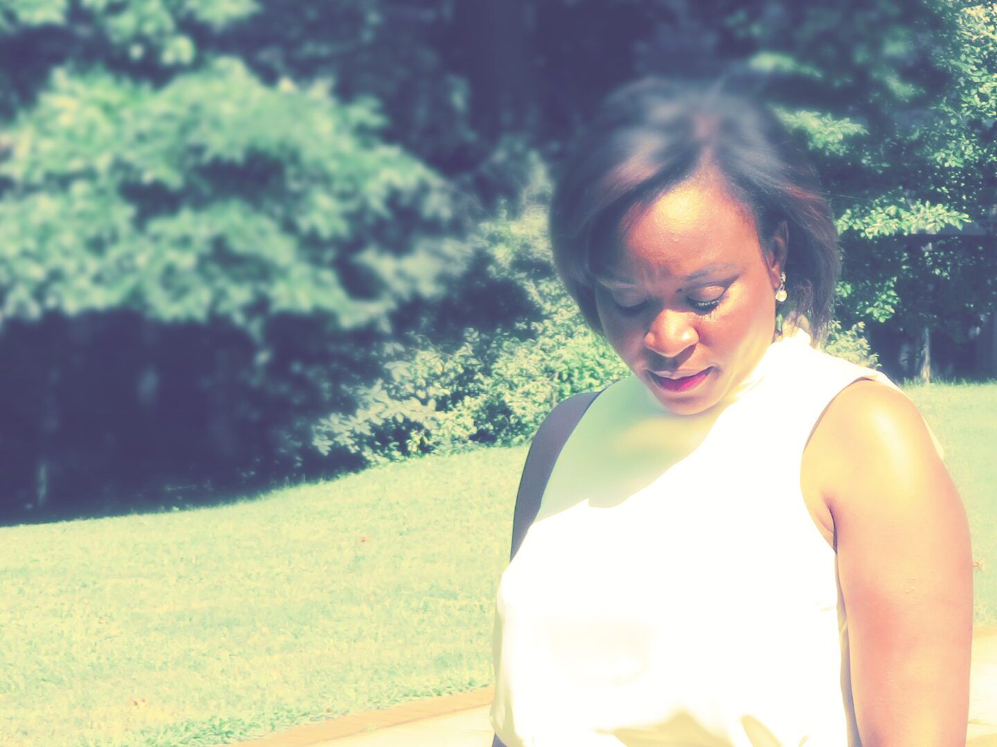 A woman in white shirt standing next to grass.