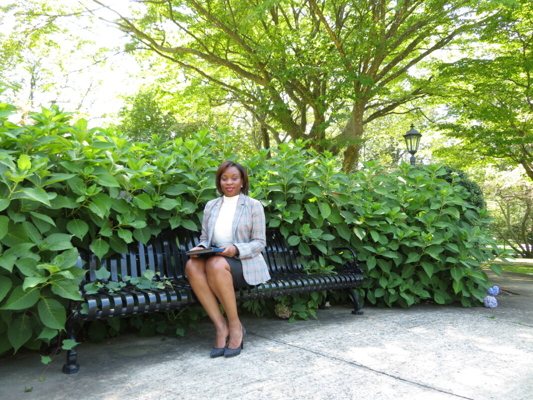 A woman sitting on top of a bench in front of bushes.